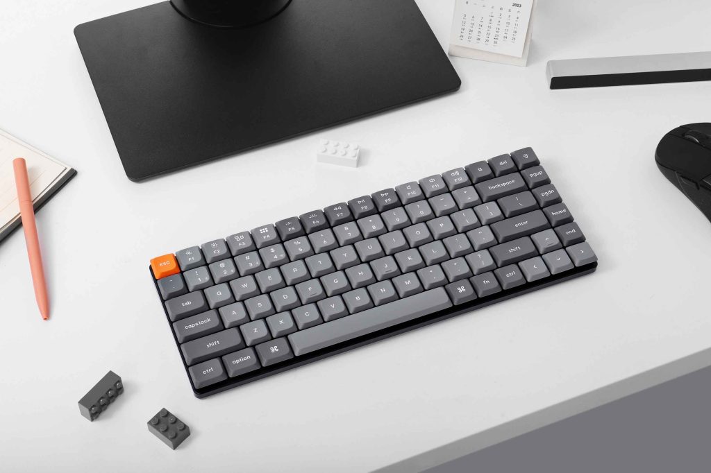 左側にMacBookでのプログラミング画面、右側にWindowsモニターでのFPSゲーム画面が表示されたデスク環境。手前中央にはKeychron K3 MAXキーボードが配置され、二刀流の使用スタイルを示している。